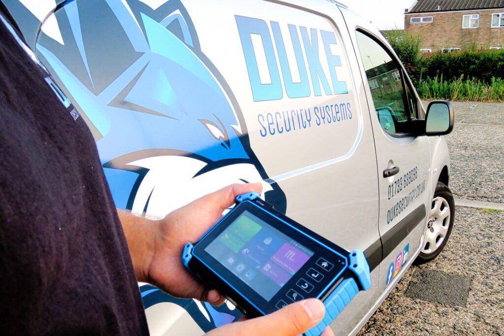 CCTV engineer using handheld tester with duke security systems van in background